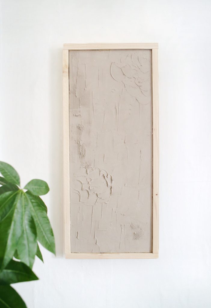 close up of plaster wall art on white wall next to plant