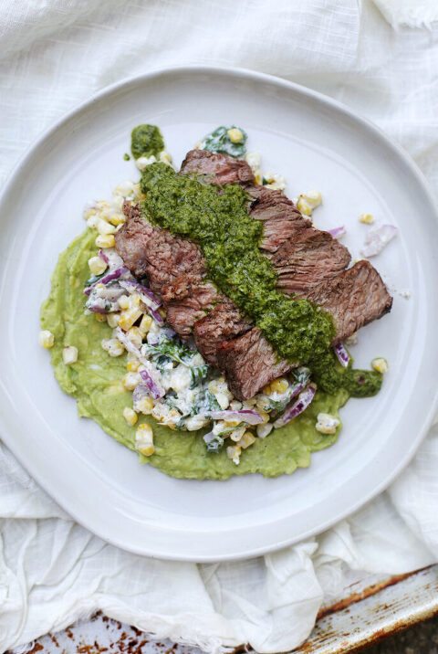 steak and chimichurri over corn salad on white plate