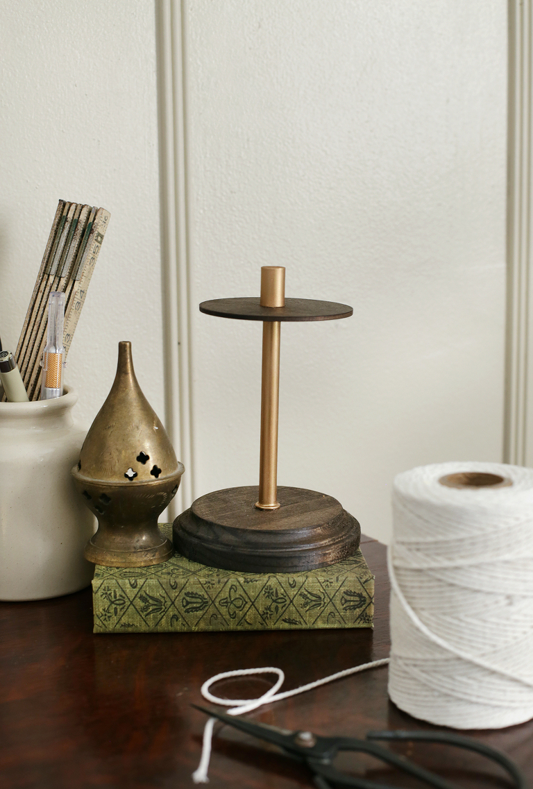 empty wood and brass twine holder on green gardening book next to brass incense holder and roll of twine