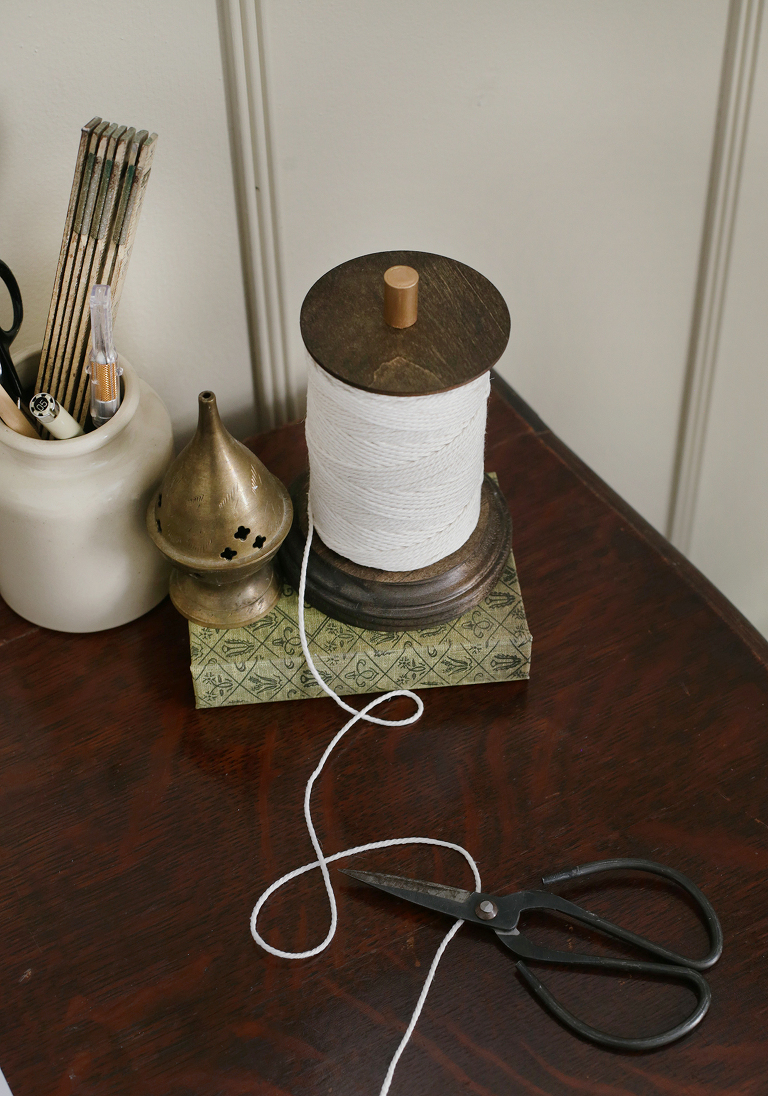 twine holder with twine unraveling on top of green book next to ceramic cup of utensils and scissors