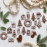 large group of gingerbread salt dough ornaments laying on white background surrounded by pine and garlands