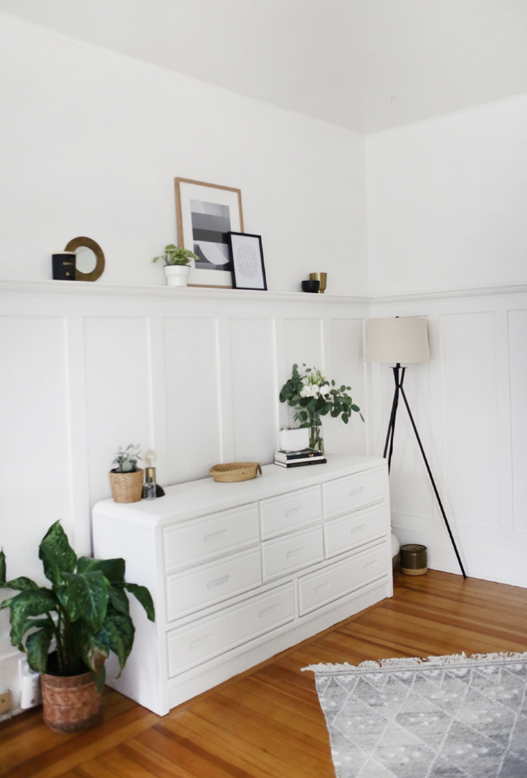 white dresser against white wall with flowers, plants, picture frames