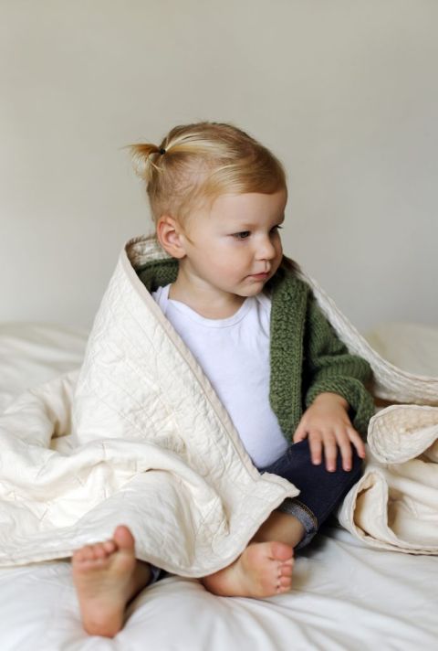 blond girl in white shirt and green sweater wrapped in simple quilted throw