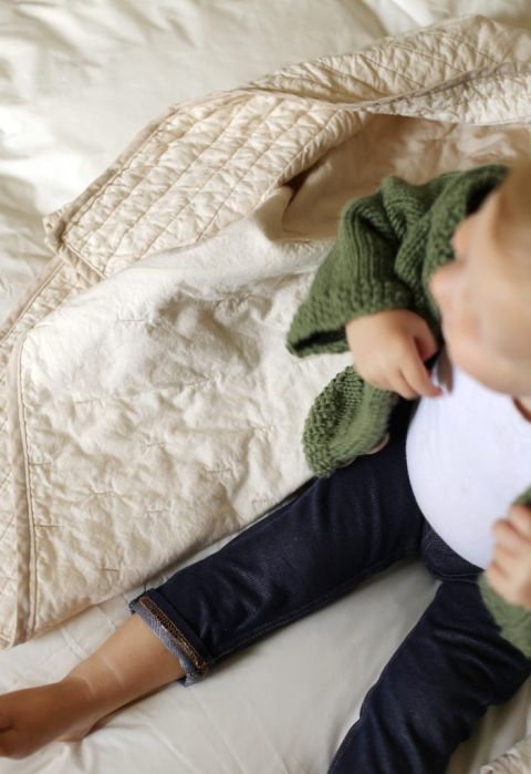 overhead shot of toddler in jeans, white shirt and green sweater surrounded by blankets