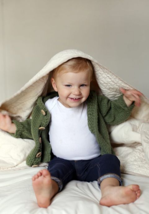 blonde toddler holding quilted throw over head with arms out to side