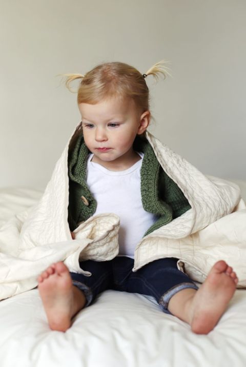 blone toddler wearing white shirt, untried sweater and jeans wrapped in surf quilted blanket