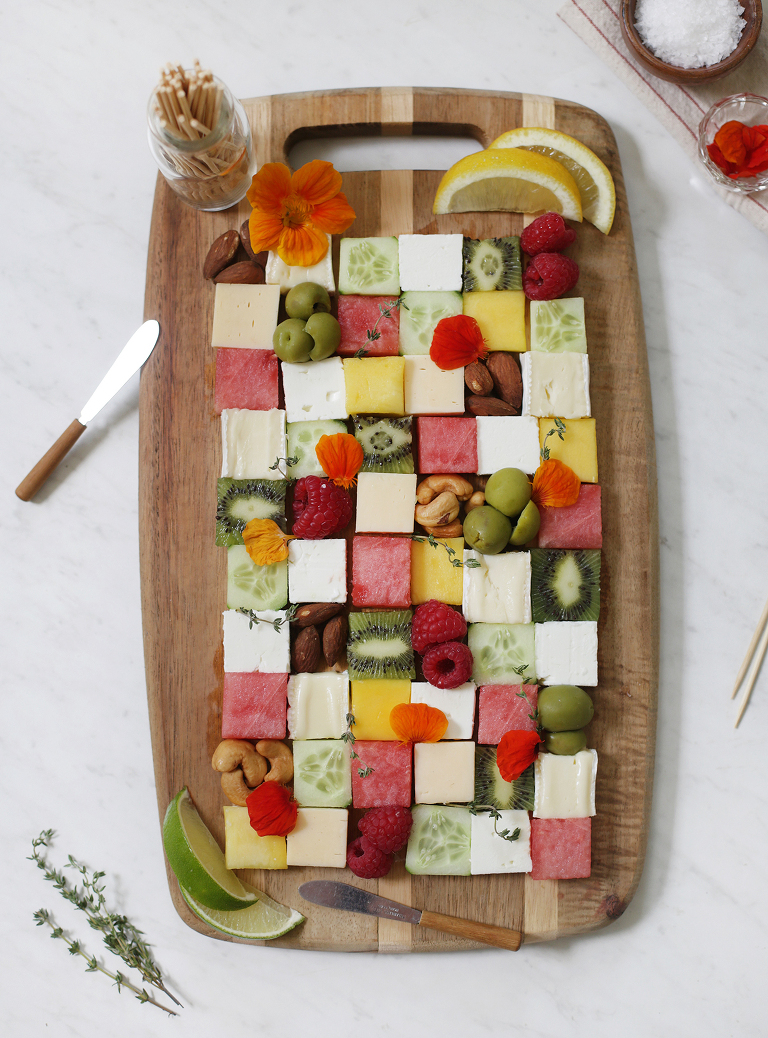 fruits and cheeses cut into squares and displayed in a checkerboard pattern on a wood cutting board