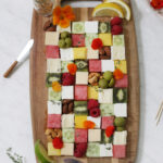 fruits and cheeses cut into squares and displayed in a checkerboard pattern on a wood cutting board