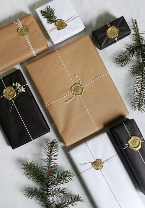 wax stamp gift wrapping on presents laid out on white surface with some pine