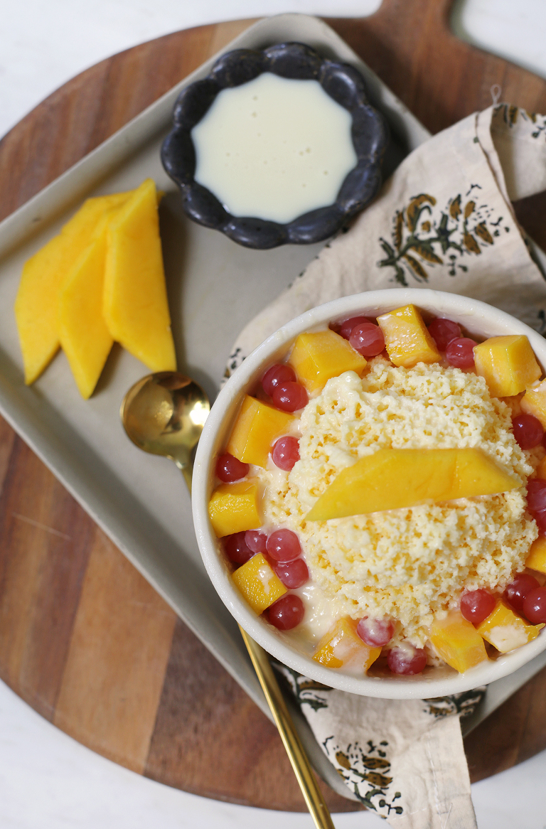 shaved mango ice in bowl with toppings on ceramic tray with fresh mango slices