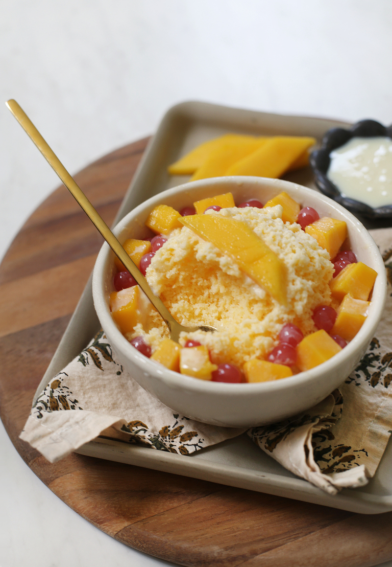 gold spoon in a bowl of mango bingsu with fresh mango and boba toppings