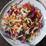 crunchy sesame salad on an off white plate surrounded by sesame seeds scattered on dark wooden table