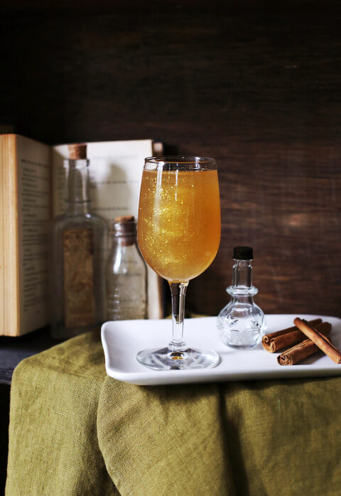 cocktail glass on plate in front of open book and assorted vials