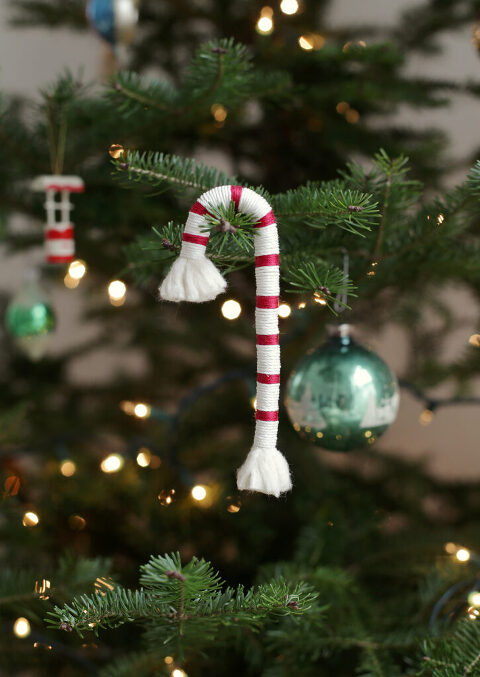 wrapped white and red cotton snacks cane hanging on christmas tree with lights and other ornaments in background