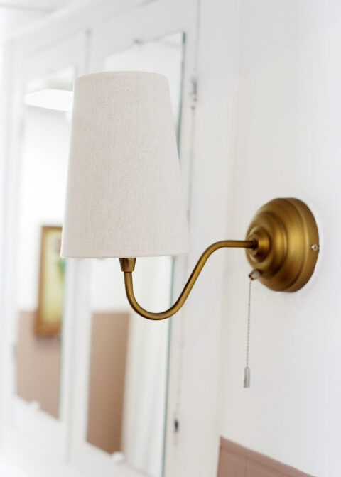 gold wall sconce with lamp shade in a white and brown bathroom