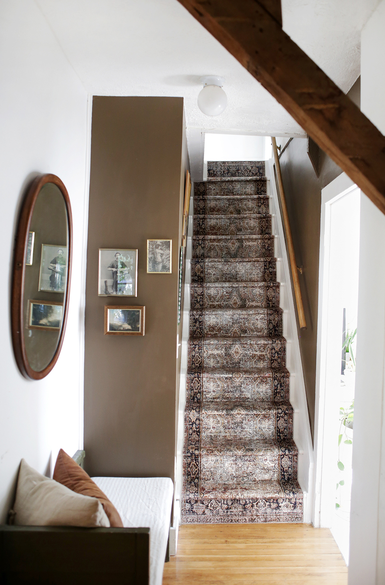 Brown and white stairwell with stair runner and vintage frames on wall