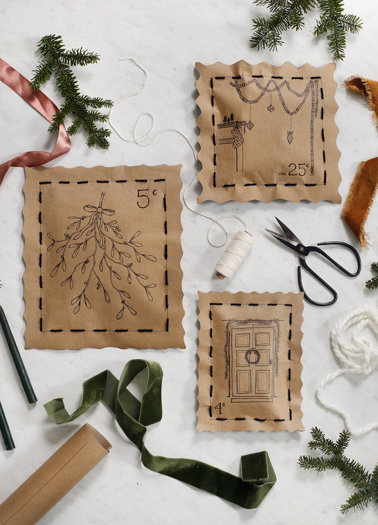 three hand stitched stamp wrapping christmas gifts surrounded by string, ribbons, and pine