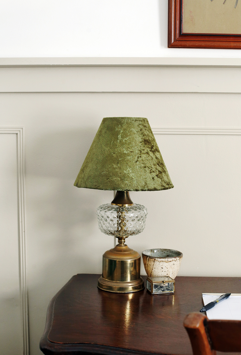 antique lamp with green lampshade on wooden desk next to ceramic container and planner