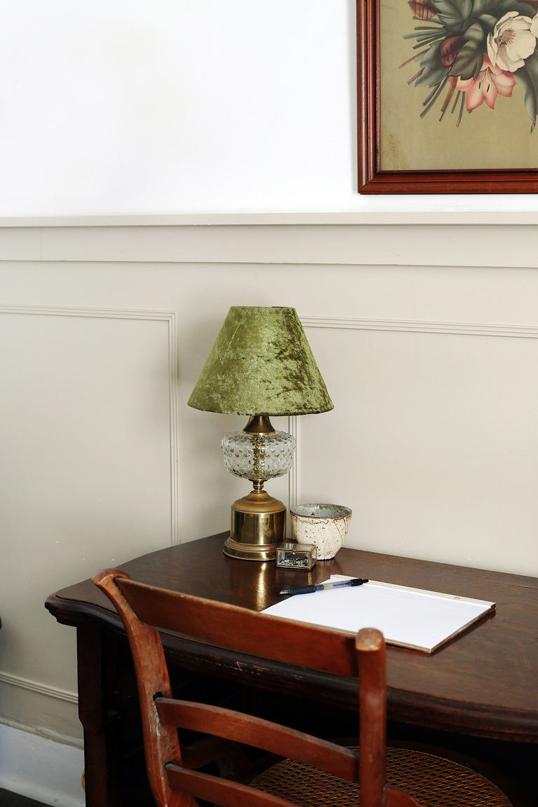 vintage lamp with green velvet lampshade on dark wooden desk next to weekly planner with pen