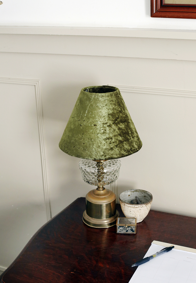 antique lamp with green lampshade on wooden desk next to ceramic container and planner