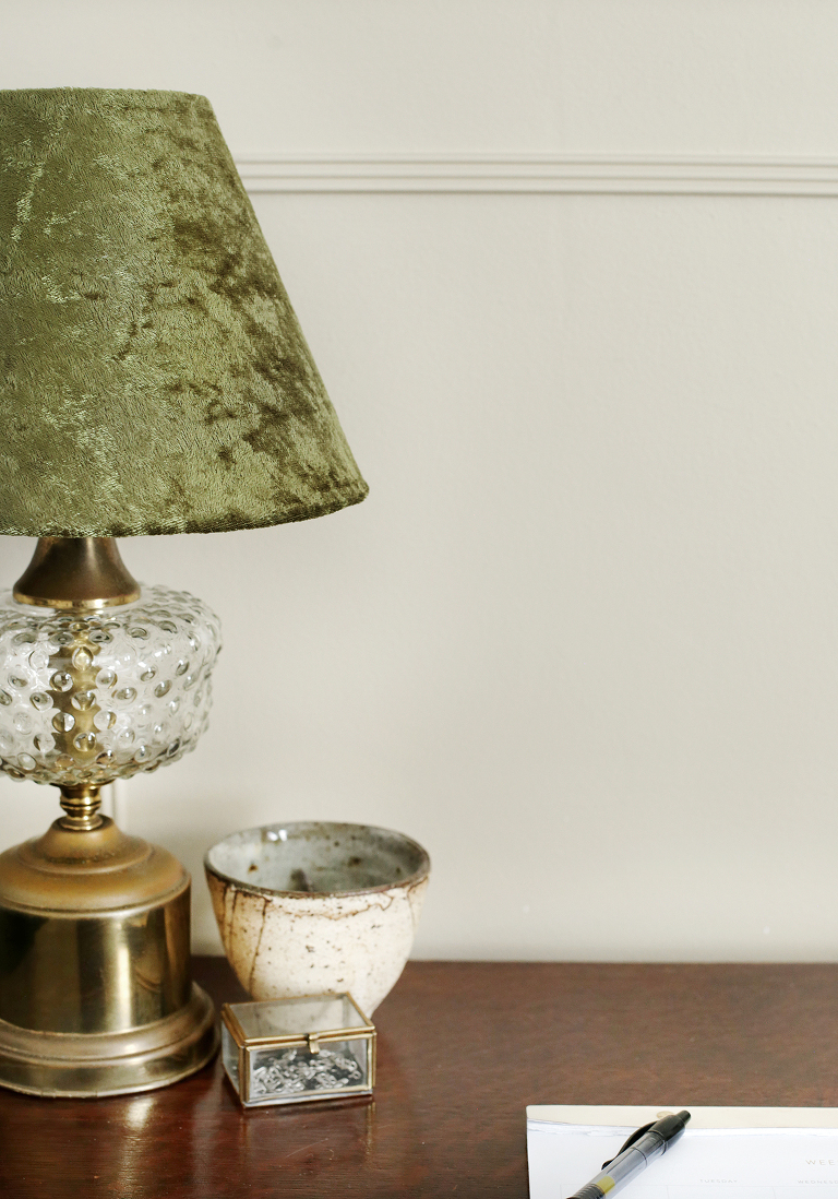 antique gold and glass lamp with green velvet lampshade on desk next to knick knacks
