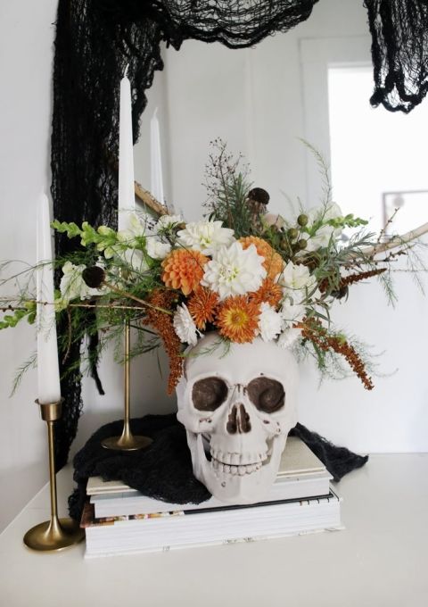 skull full of greens and orange flowers on top of magazine stack