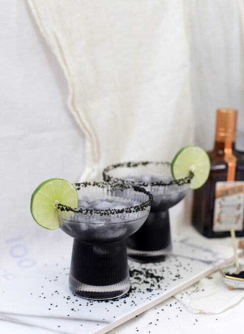two cocktail glasses in front of cloth backdrop