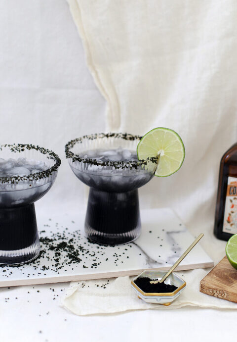 margaritas on marble slab with black sugar spilled around it