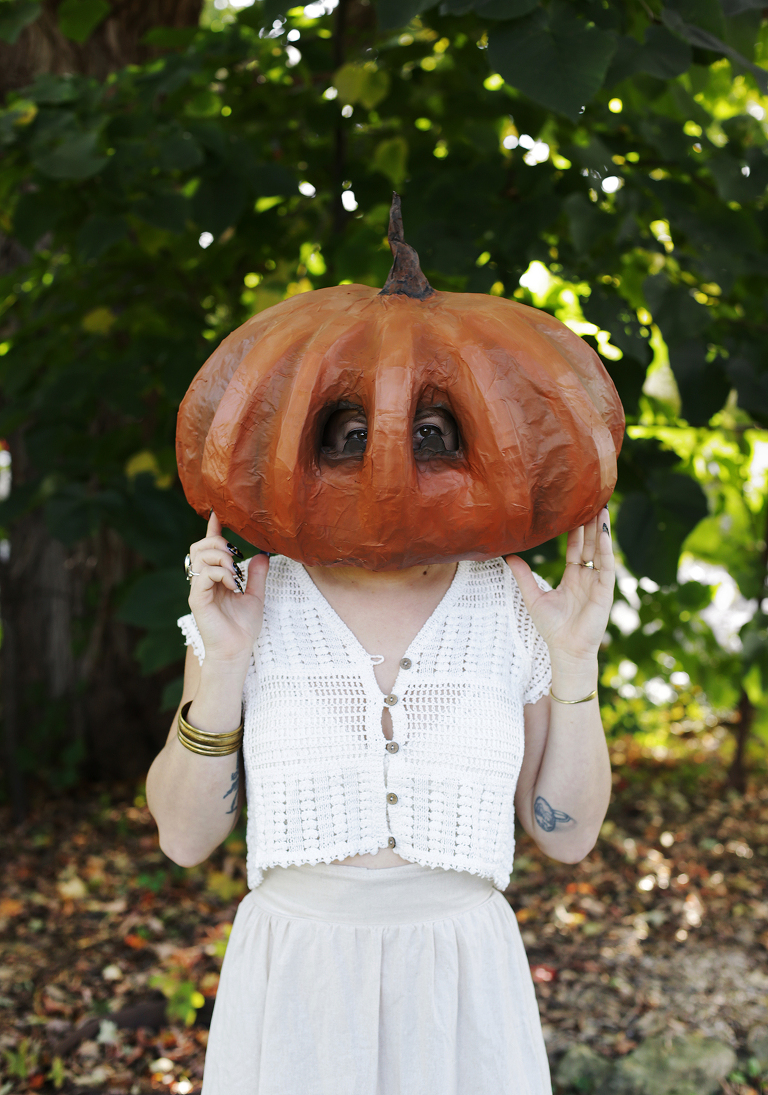 girls wearing white crochet top and reaching up and holding paper mache mask