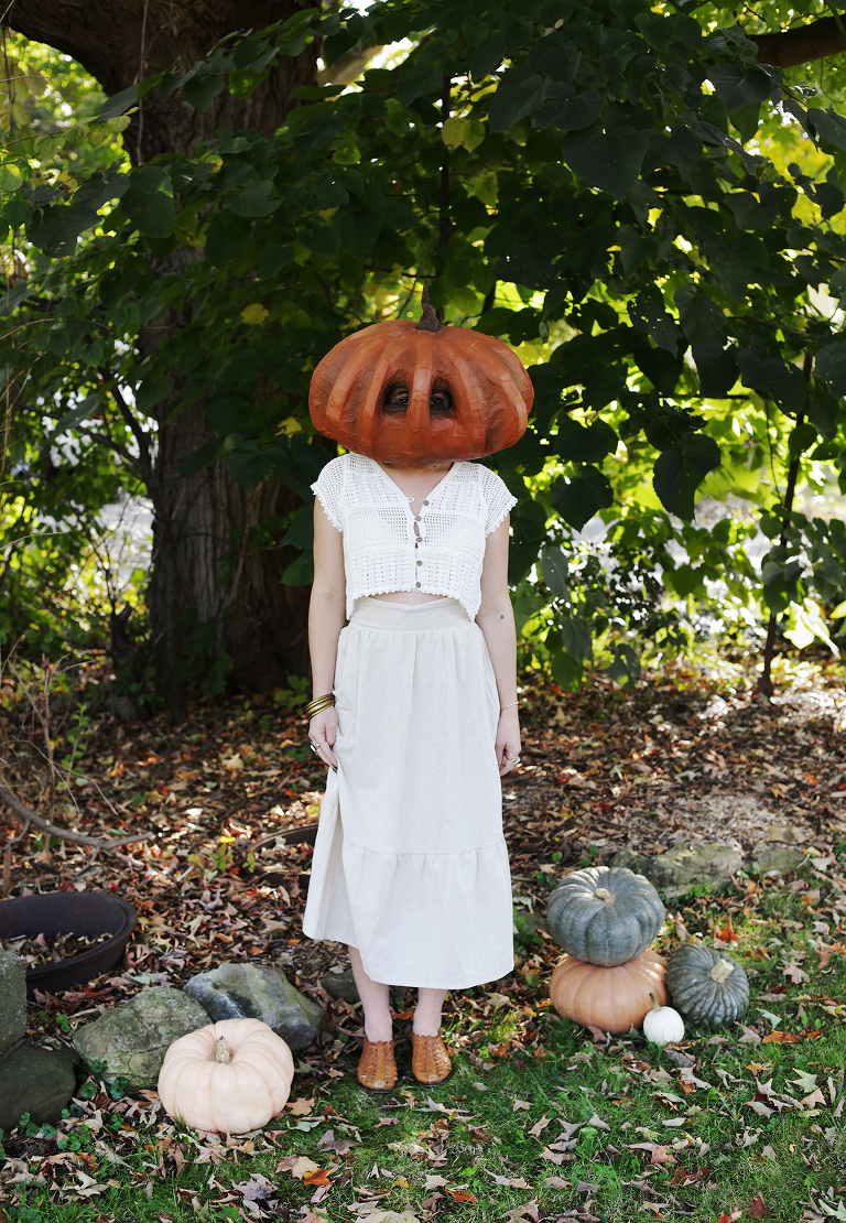 girl wearing halloween costume outside in garden with pumpkins around her