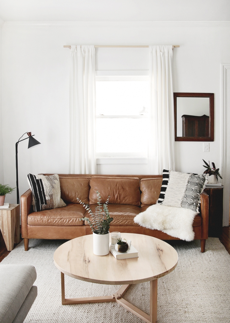 brown leather couch with round coffee table and white curtains behind couch