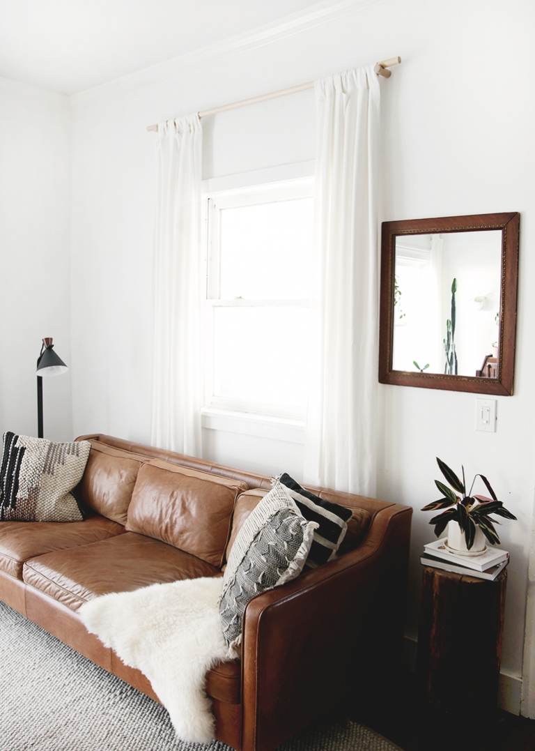 leather couch against white curtains with brown framed mirror on wall