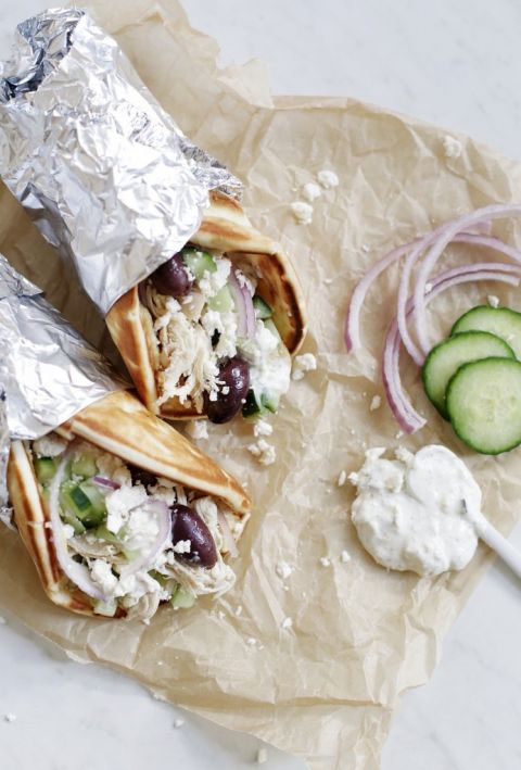 two chicken gyros on parchment paper with toppings next to it