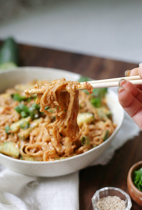 hand holding chopsticks lifting peanut noodles out of bowl