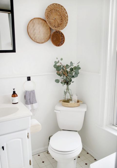 white bathroom corner with toilet, vase of eucalyptus, baskets on the wall
