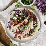 three tacos on a plate surrounded by raw ingredients