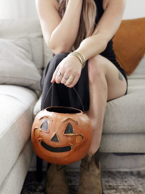 woman holding pumpkin treat bucket while sitting on beige couch