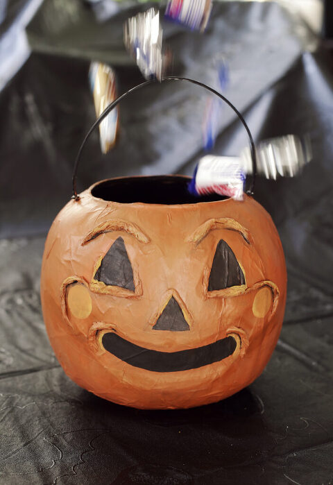 candy falling into paper mache pumpkin treat bucket on black backdrop