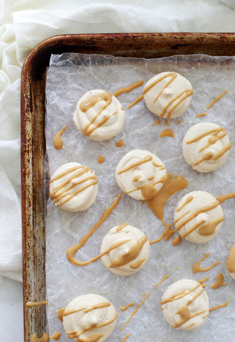 frozen peanut butter whips drizzled with peanut butter on top of a parchment lined cookie sheet