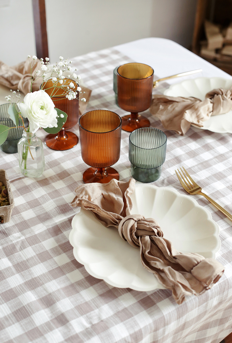 tied linen napkin on scalloped cream plate with amber and green glassware and brown gingham tablecloth