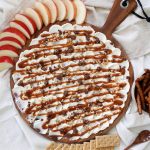 round cutting board with cream cheese and caramel spread on top surrounded by snacks
