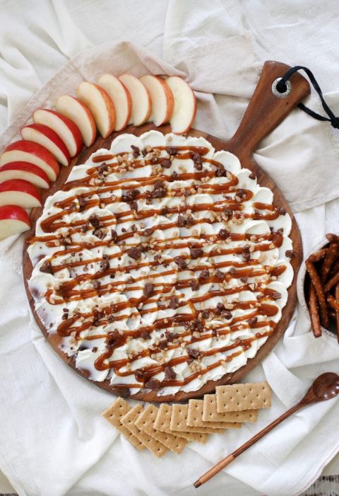 round cutting board with cream cheese and caramel spread on top surrounded by snacks