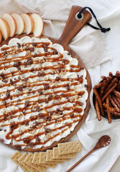 round cutting board with caramel cream cheese spread on top surrounded by snacks