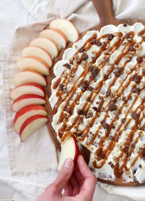 hand holding apple slice, scooping cream cheese and caramel dip off cutting board