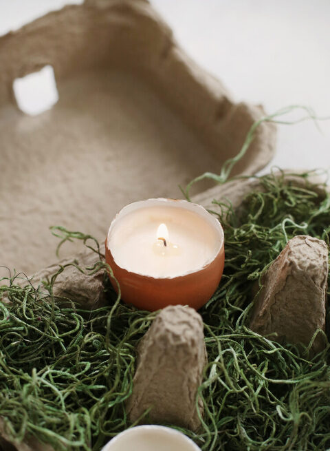 close up of egg candle with wick burning set on top of moss in egg carton