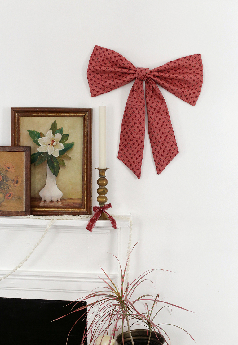 large pink fabric bow next to mantel with vintage floral art in frames and brass candle holder