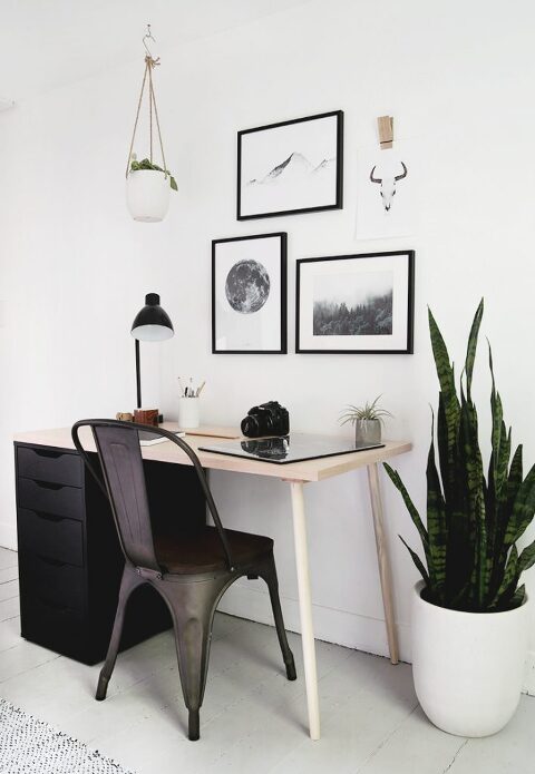 wood desk with black drawers and framed prints hanging above