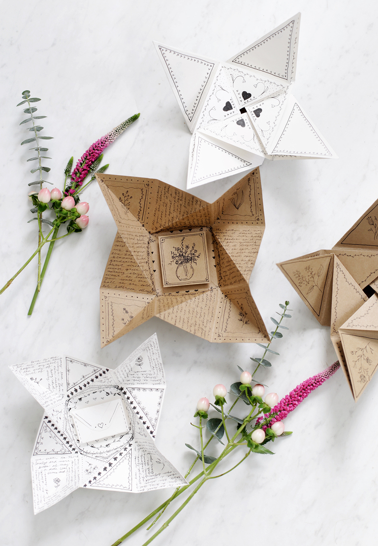 opened origami cards with black doodles laid out on marble table with pink florals