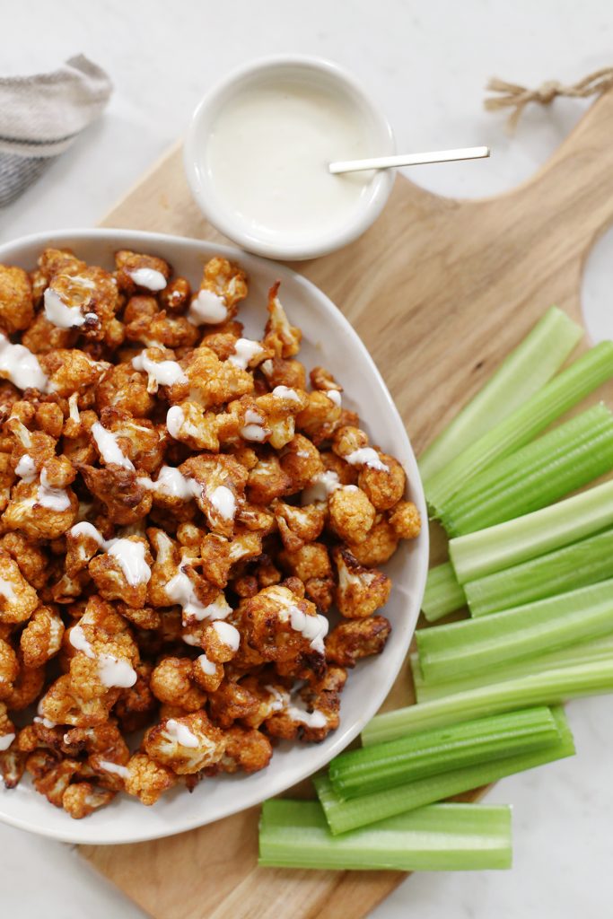 plate of buffalo cauliflower on a cutting board surrounded by celery and dressing