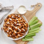 buffalo cauliflower on white plate with celery and blue cheese beside it